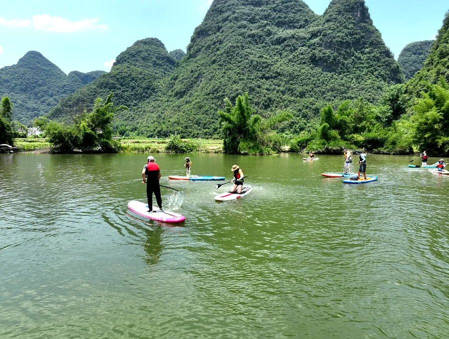 Travelers paddleboarding on the Yulong River beneath karst peaks, Yangshuo China